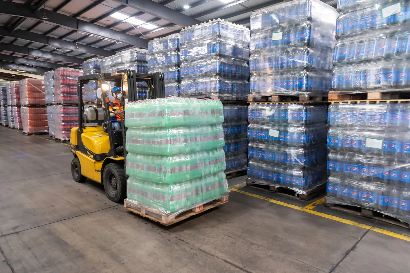 A forklift moving stacked pallets in a distribution warehouse