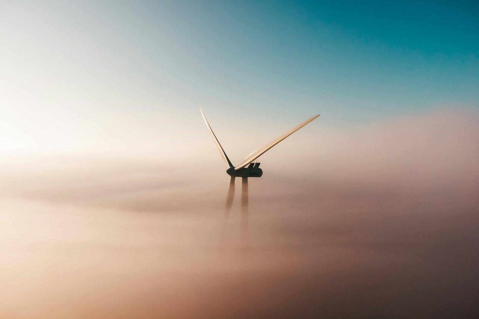 A single wind turbine emerging from sea fog at sunrise